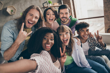 Photo portrait of smiling students showing v-sign heavy metal gestures taking selfie sitting on sofa