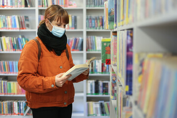 woman with mask reading book in library during covid-19 pandemic time