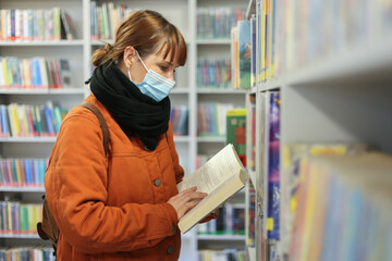 woman with mask reading book in library during covid-19 pandemic time close up