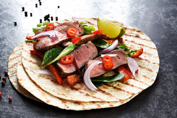 Grilled beef steak. Fajitos, tortillas with salsa, chili and beef on a dark background.