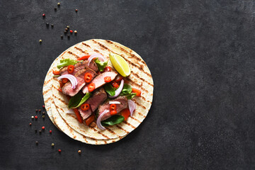Grilled beef steak. Fajitos, tortillas with salsa, chili and beef on a dark background.