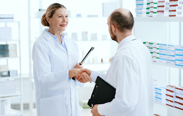female pharmacist greets a colleague with a handshake.