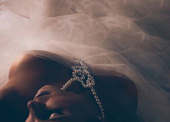 Overhead view of a seductive woman wearing a pearl necklace and tulle fabric