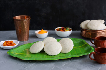 Many Idli idly sambar coconut chutney , tomato chutney serving breakfast vegetarian food South Indian restaurant on banana leaf plate Kerala Tamil Nadu India Sri Lanka. healthy steamed rice cakes .