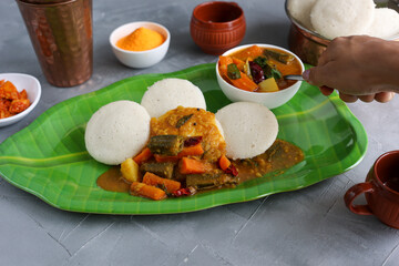 Many Idli idly sambar coconut chutney , tomato chutney serving breakfast vegetarian food South Indian restaurant on banana leaf plate Kerala Tamil Nadu India Sri Lanka. healthy steamed rice cakes .