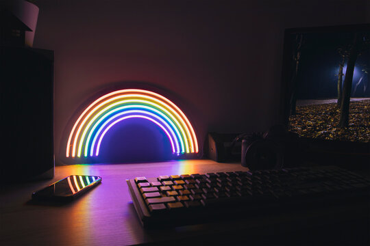 Modern workspace with pc and neon rainbow on the table  in the evening