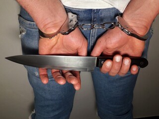 Murderer with handcuffs on hands holding knife, arrested man holding knife