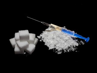 Injection syringe on cocaine drug powder pile and lump sugar cubes on black background, sugar is more addictive than cocaine, isolated cubes of white sugar and cocaine on black background