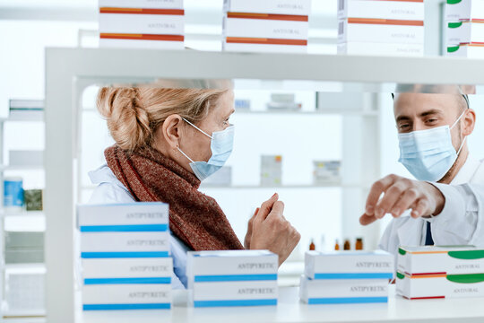 Pharmacist And A Customer In Protective Masks Are Talking Near A Pharmacy Window.