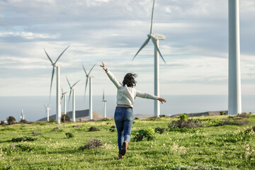 Unrecognizable woman running in meadow with windmills