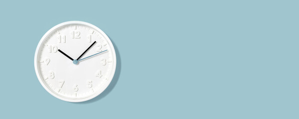 White plain analogue wall clock on trendy pastel blue background. Five past ten o'clock. Close up...