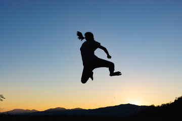 Fototapeta na wymiar Silhouette of happy child jumping playing on mountain at sunset or sunrise