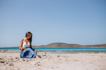 gorgeous style brunette young woman in blue chameleon dress long train and white top sits on a rock near the sea, sand tropical on a rock.beautiful mermaid lonely melancholy waiting freedom 