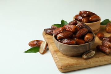 Board with bowls of dried dates on white background