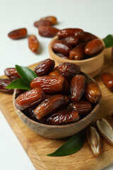 Board with bowls of dried dates on white background