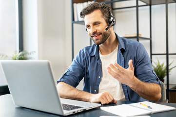 Confident man with handsome stubble, wearing headset, talking in front of computer, wearing casual...