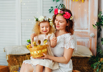 Easter composition. Mother and daughter in white dresses and flower wreaths on their heads play with ducklings. Farm village village holiday. Children and pets