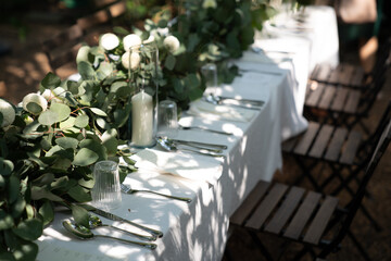 Wedding table decorated with white flower, candle in glass vase and green leaf on white tablecloth. composition of greenery. copy space . wedding ceremony