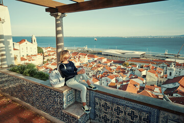 Traveling by Portugal. Young traveling woman enjoying old town Lisbon view, red tiled roofs,...