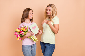 Photo of blonde haired mother and small girl kid wear jeans hold card flowers celebrate isolated on beige color background