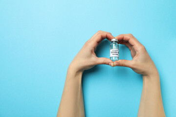 Female hands hold vial of Covid - 19 vaccine on blue background