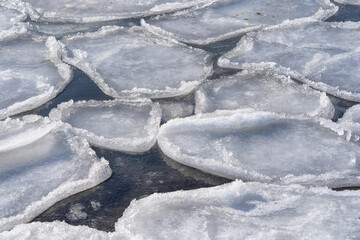 Spring background with melting ice on the surface of a frozen bay. Snowy shore of a frozen lake.