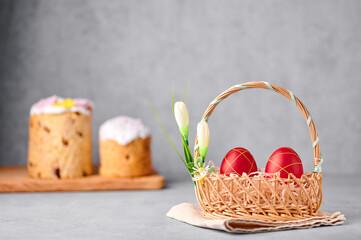Two red painted Easter eggs in the wicker basket on gray table top with two easter cakes on backdrop