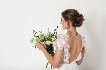 Young bride wearing wedding dress with beautiful bouquet on light background