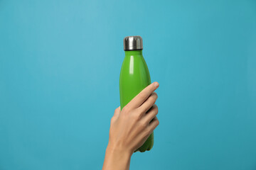 Woman holding modern green thermos on light blue background, closeup