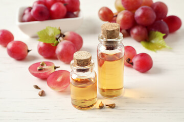 Organic red grapes, seeds and bottles of natural essential oil on white wooden table