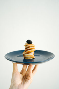 Man's hand holding a plate with a stack of miniature pancakes topped with blackberries