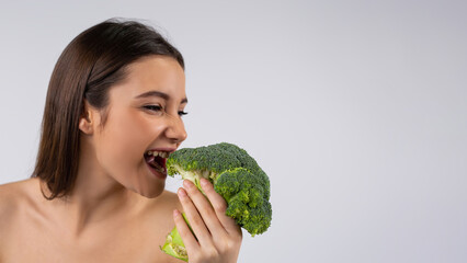 Banner, grey background. Brunette bite a fresh green broccoli. Pretty young with a green vegetable....