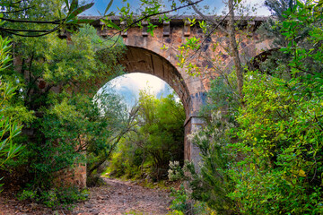 Old railway bridge surrounded by green and lush vegetation. Railroad in disuse immersed in the wild forest. Wonderful green path. Secret routes in a uncontaminated land. Breathtaking landscapes view.