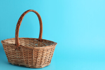 Fototapeta na wymiar Empty wicker basket on light blue background, space for text. Easter item