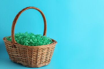 Fototapeta na wymiar Easter basket with green paper filler on light blue background, space for text