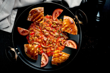 Turkish lamb goulash in red sauce with bell pepper and traditional buns in a metal dish on a black background. Close up, selective focus