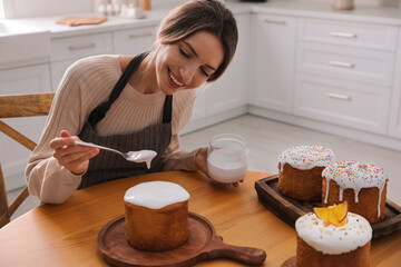 Young woman decorating traditional Easter cake with glaze in kitchen