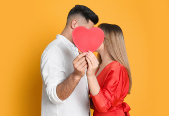 Lovely couple kissing behind decorative heart on yellow background. Valentine's day celebration