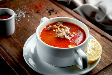 Red Turkish soup with lamb and vegetables in a white plate on a wooden tray. Dark background