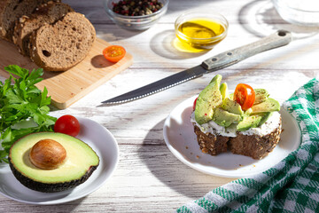 Avocado toast on white wooden base with shadows from the kitchen window.