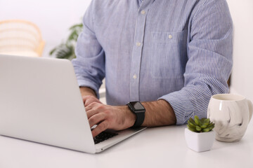 Young man with smart watch working on laptop at table in office, closeup