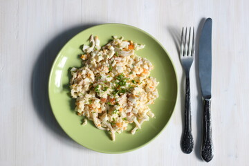 squid salad with mayo, rice, egg, onion in green plate and cutlery on white wooden table