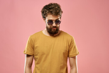 Cute bearded man in a yellow T-shirt dark glasses pink background