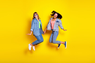 Fototapeta na wymiar Full length portrait of charming cheerful ladies hold each other arm have fun isolated on yellow color background