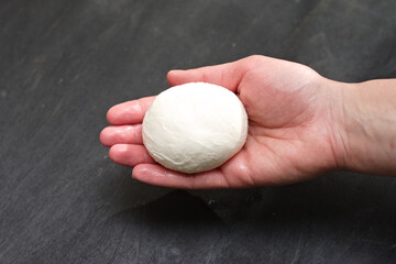 A lump of freshly made mozzarella cheese in a female palm on a black background with a dark shadow