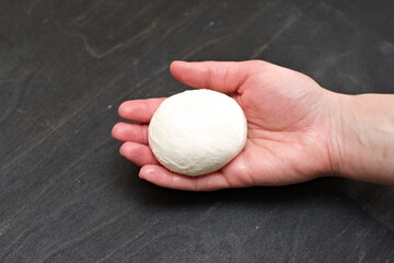 Piece of freshly made mozzarella cheese in a female palm on a black background with a dark shadow