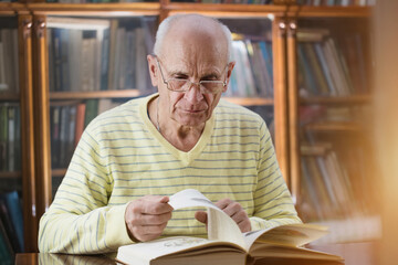 Mature professor wearing eyeglasses sitting at table and leaf through old book.