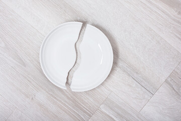 Broken white plate on the wiooden grey floor