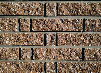 The texture of an old wall made of brown chipped decorative uneven bricks interspersed with light...