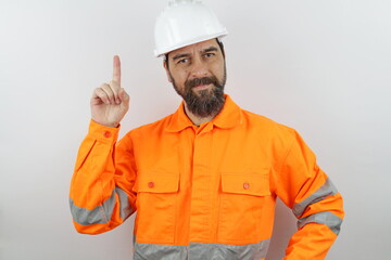 Handsome man with beard wearing worker uniform and hardhat showing pointing up finger number one while smiling onfident happy